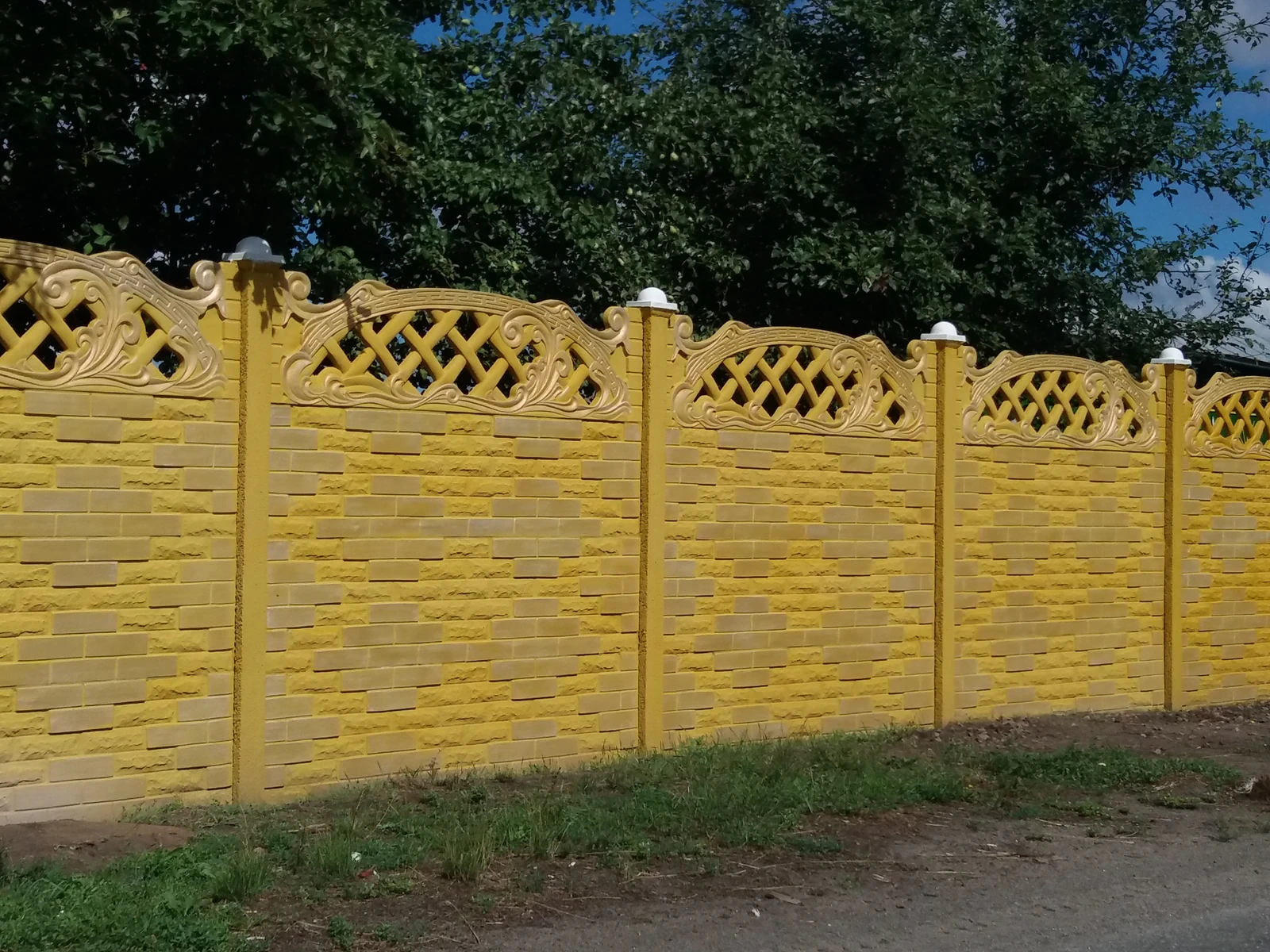 Декоративний бетонний паркан жовтого кольору з ажурними верхніми елементами