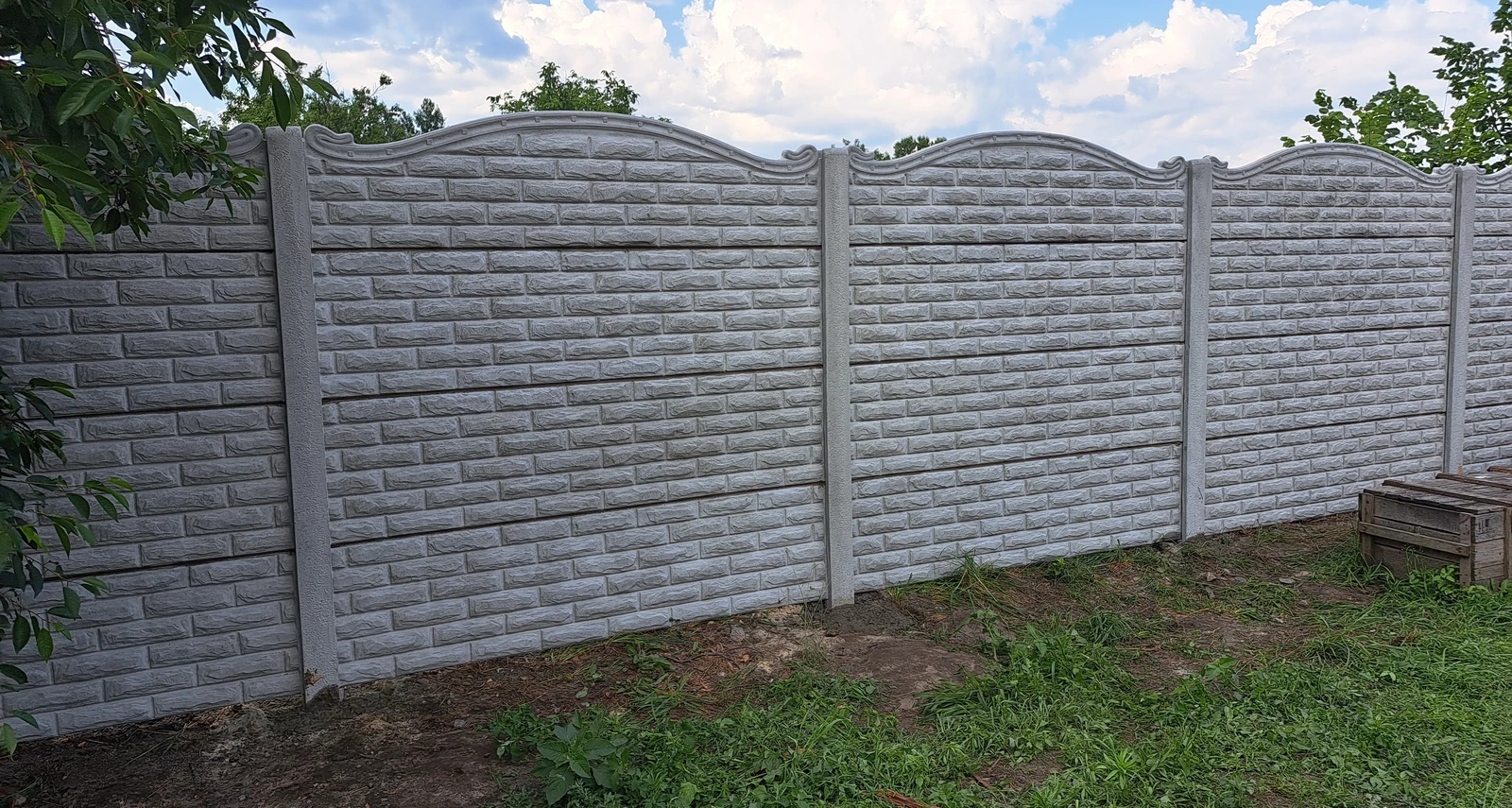 Встановлена бетонна огорожа з декоративною верхівкою та фактурою під цеглу на приватній ділянці.